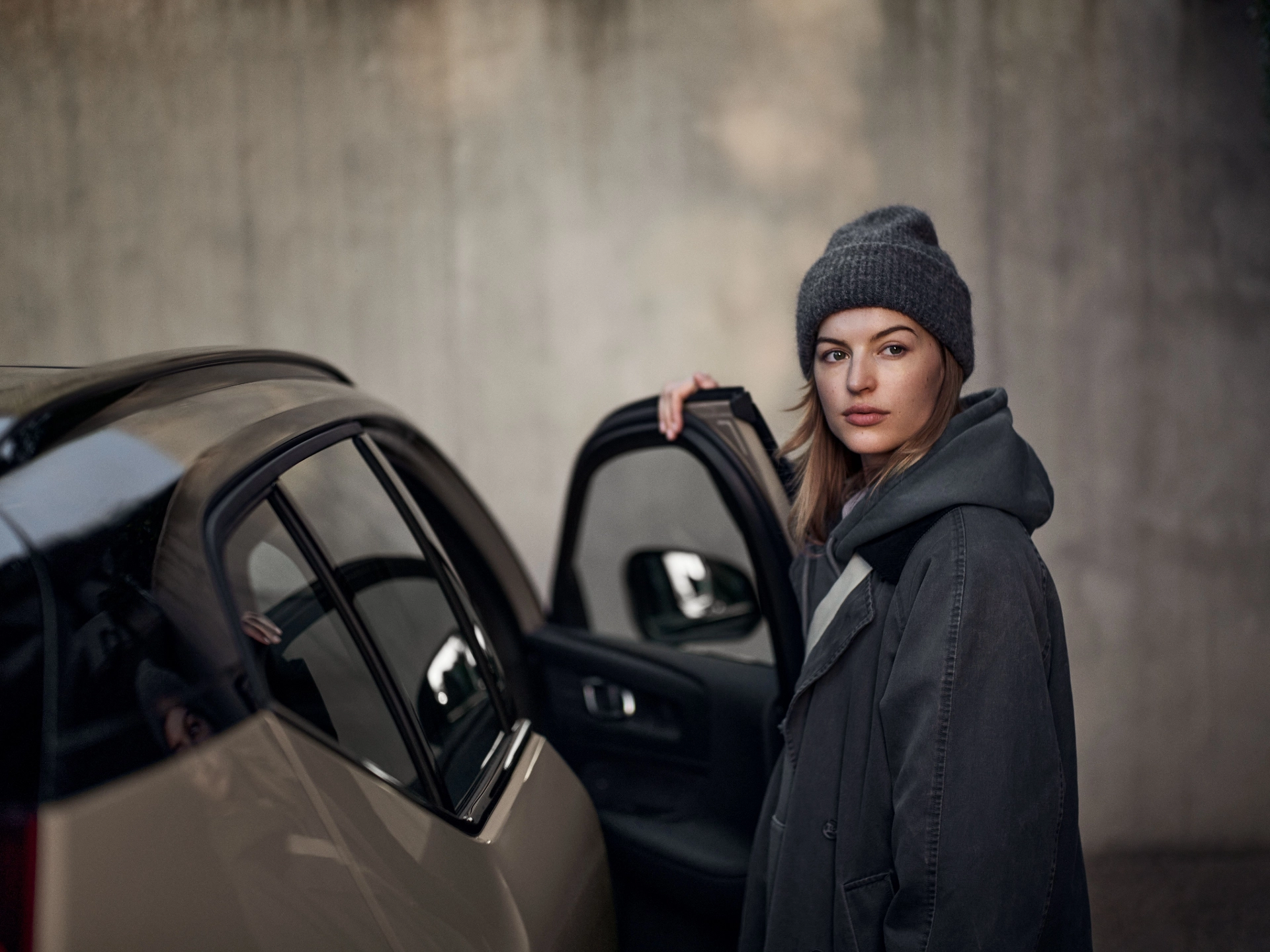 Mujer joven con abrigo al lado de un vehículo híbrido Volvo.